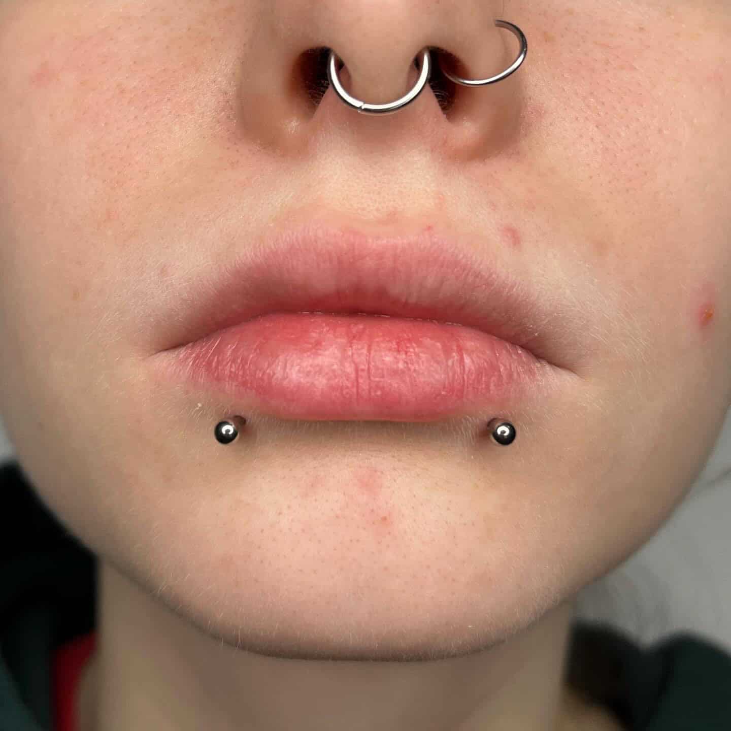 7sinstattoo.live Zbliżenie ust i nosa osoby, ozdobionych dwoma srebrnymi kółkami w nozdrzach i piercingiem przegrody nosowej, a także dwoma piercingami dolnej wargi z małymi srebrnymi kulkami. Skóra ma kilka skaz. Podobną sztukę na ciele znajdziesz w 187A4CCE-E865-44DB-B1A0-684BEFC77F61 w studio tatuażu Poznań, znanym jako najlepsze studio tatuażu Poznań. Najlepsze studio tatuażu Seven Sins Tattoo