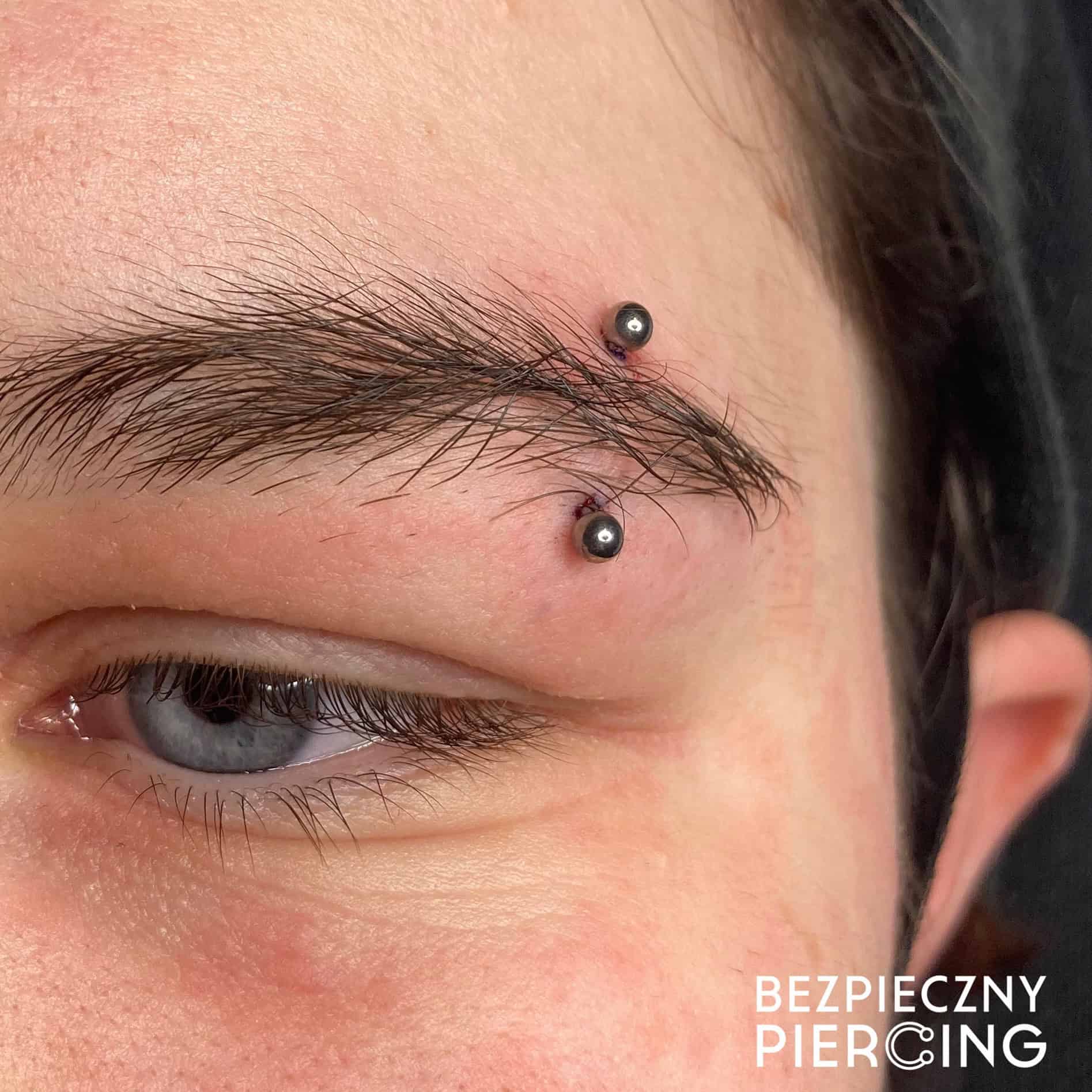 7sinstattoo.live Zbliżenie brwi osoby ze świeżym poziomym piercingiem z dwoma czarnymi koralikami na każdym końcu. Skóra wokół piercingu jest lekko zaczerwieniona. Tekst „BEZPIECZNY PIERCING” jest widoczny w prawym dolnym rogu, podkreślając kompetencje najlepszego studia tatuażu Poznań i prezentując ich produkt, 624DB3A9-BF17-4CB5-8ADA-3FE1C3E632F1. Najlepsze studio tatuażu Seven Sins Tattoo