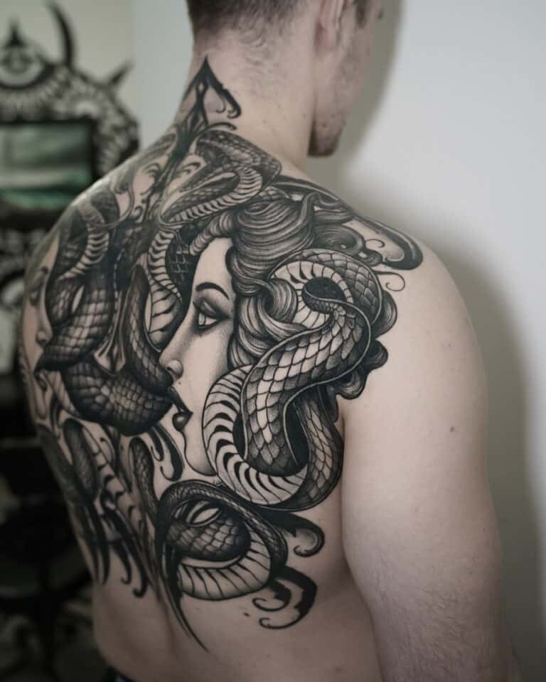 7sinstattoo.live Osoba z dużym, szczegółowym tatuażem na plecach, przedstawiającym twarz kobiety przeplataną kilkoma realistycznie wyglądającymi wężami, wybrała DSC03480 ze względu na skomplikowane cieniowanie i faktury. Tatuaż rozciąga się od ramienia do ramienia i w dół do dolnej części pleców, prezentując kunszt najlepszego studia tatuażu Poznań. Najlepsze studio tatuażu Seven Sins Tattoo