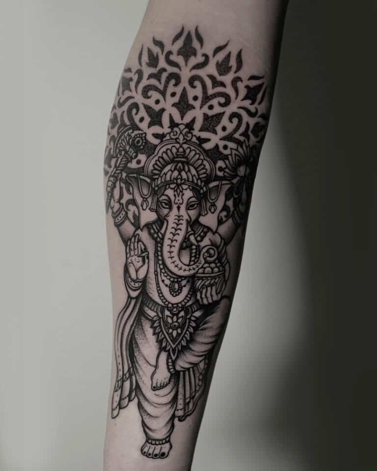 7sinstattoo.live Tatuaż na przedramieniu, przedstawiający czarno-szarą interpretację hinduskiego bóstwa z głową słonia, Ganeshy, prezentuje skomplikowany wzór o nazwie DSC04784. Został stworzony przez artystę z wiodącego studia tatuaży Poznań i zawiera ozdobne detale wokół bóstwa oraz elementy dekoracyjne nad głową Ganeshy. Najlepsze studio tatuażu Seven Sins Tattoo
