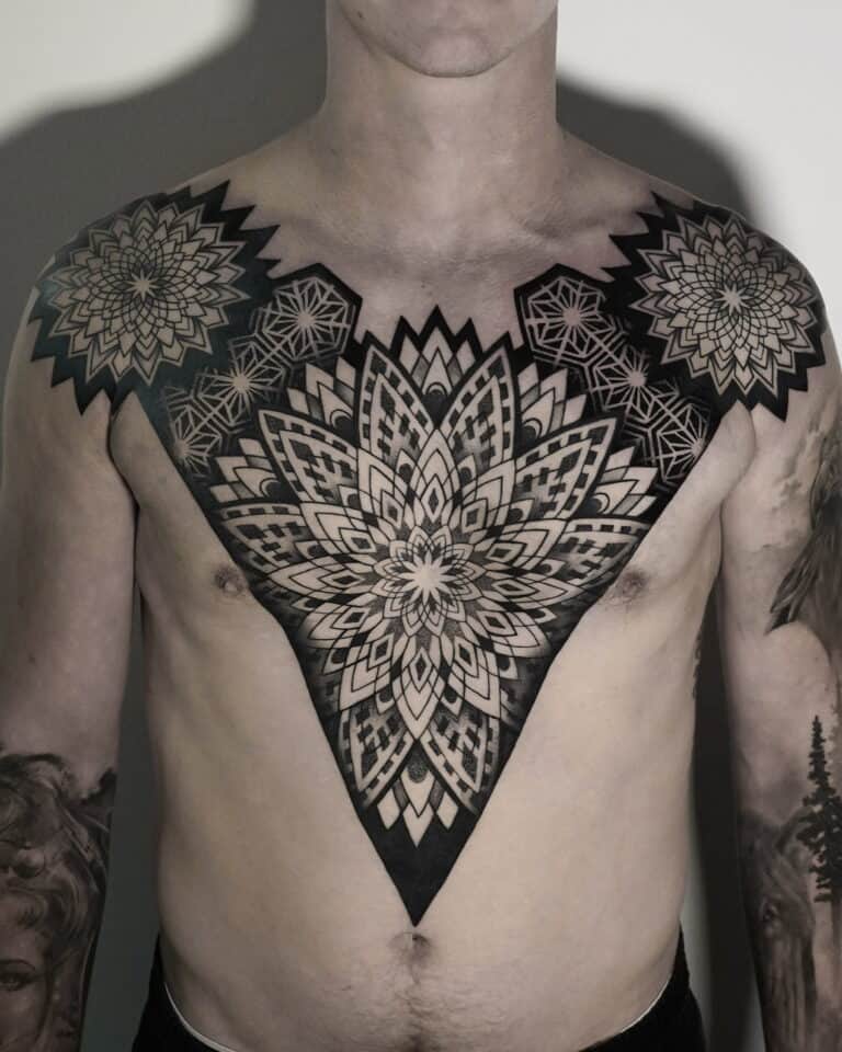 7sinstattoo.live Osoba z misternymi czarnymi geometrycznymi tatuażami pokrywającymi klatkę piersiową i ramiona, które zostały wykonane w najlepszym studio tatuażu w Poznaniu. Centralny wzór przedstawia duży, symetryczny wzór kwiatowy, podczas gdy mniejsze sąsiadujące wzory uzupełniają go na ramionach. Ta szczegółowa i symetryczna sztuka ciała została uchwycona w produkcie DSC04820. Najlepsze studio tatuażu Seven Sins Tattoo