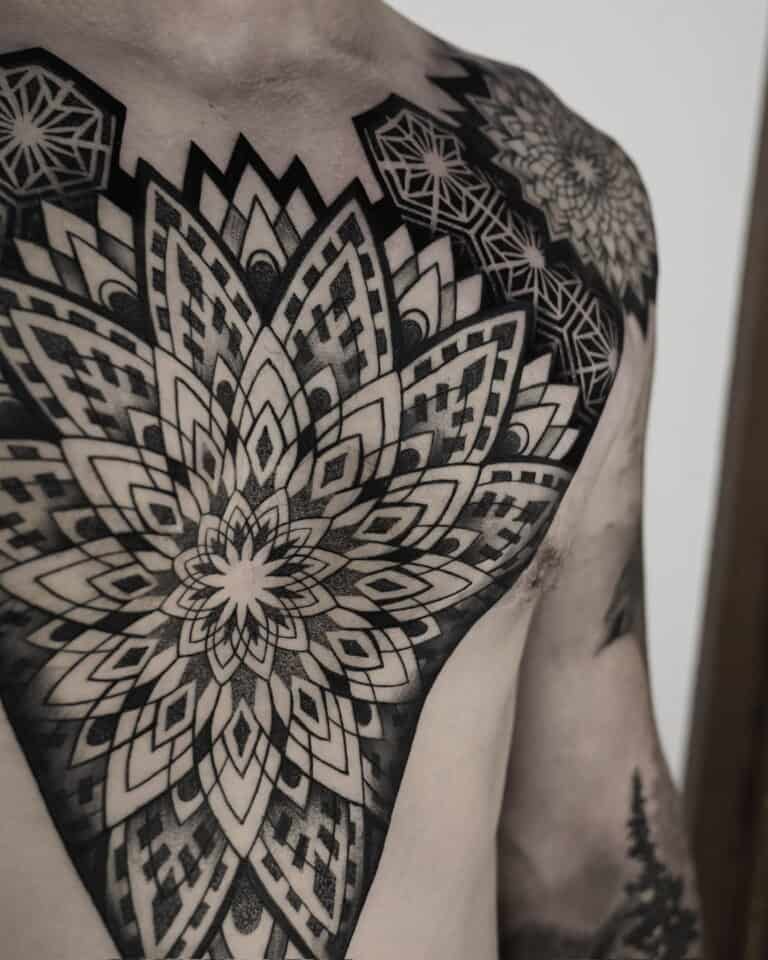 7sinstattoo.live Zbliżenie górnej części klatki piersiowej i ramion osoby prezentuje rozległy i skomplikowany geometryczny wzór tatuażu z najlepszego studia tatuażu Poznań, zidentyfikowanego po nazwie produktu DSC04832. Tatuaż charakteryzuje się symetrycznymi wzorami i kształtami przypominającymi mandalę z czarnym i szarym cieniowaniem, pokrywającymi znaczną część skóry. Najlepsze studio tatuażu Seven Sins Tattoo