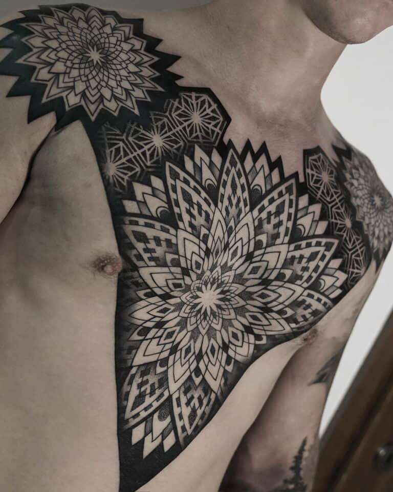 7sinstattoo.live Osoba z misternymi czarno-szarymi geometrycznymi tatuażami mandali DSC04864 na klatce piersiowej i ramieniu, wykonanymi w najlepszym studio tatuażu w Poznaniu. Tatuaże składają się z warstwowych, symetrycznych wzorów o różnych kształtach i cieniowaniu, pokrywających jedno ramię i rozciągających się na górną część klatki piersiowej. Najlepsze studio tatuażu Seven Sins Tattoo