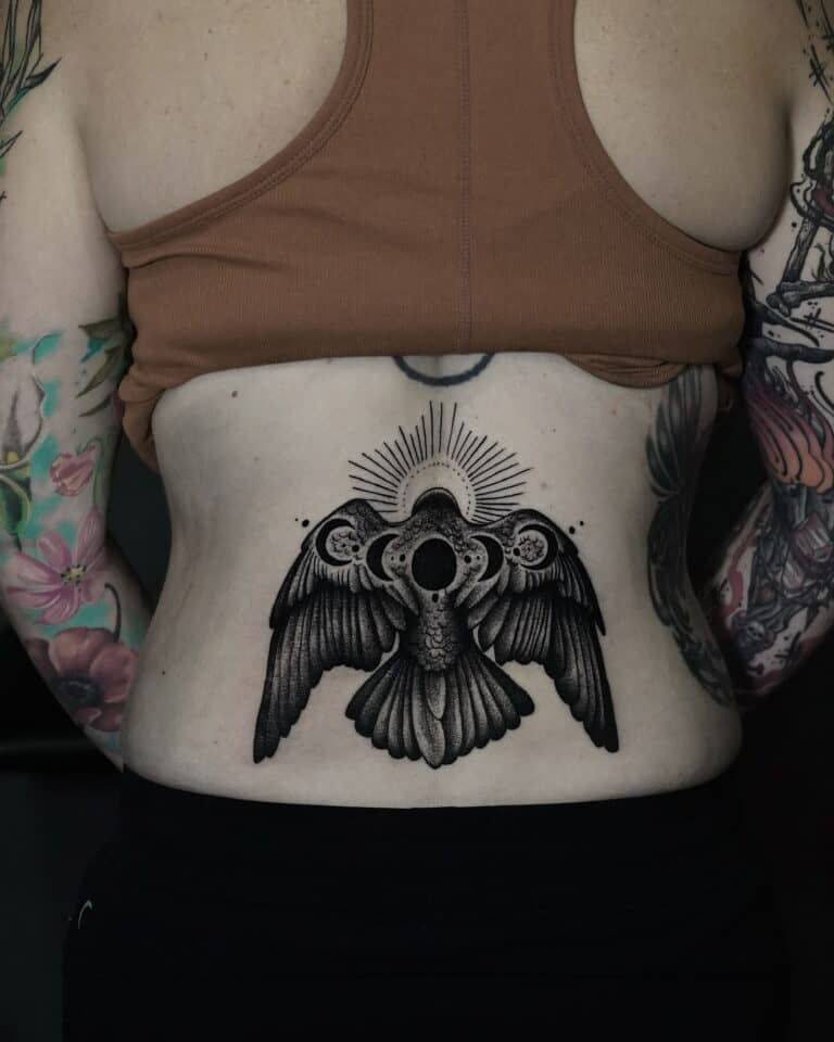 7sinstattoo.live Osoba oznaczona jako DSC05694 ma tatuaż na plecach przedstawiający szczegółowego, ciemno cieniowanego ptaka z rozpostartymi skrzydłami, okrągłym wzorem przypominającym słońce nad głową i misterną kropką. Ma na sobie brązowy krótki top i ciemne spodnie, odsłaniając kolorowe tatuaże na ramionach wykonane w najlepszym studiu tatuażu Poznań. Najlepsze studio tatuażu Seven Sins Tattoo