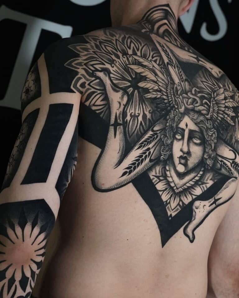 7sinstattoo.live Osoba z misternym tatuażem pokrywającym ramię i górną część pleców, wykonanym w studio tatuażu Poznań, prezentuje projekt DSC05919. Tatuaż przedstawia szczegółową twarz z misternym nakryciem głowy i ozdobnymi wzorami rozciągającymi się na ramieniu i ramieniu, obejmującymi śmiałe, geometryczne wzory i elementy kwiatowe. Najlepsze studio tatuażu Seven Sins Tattoo