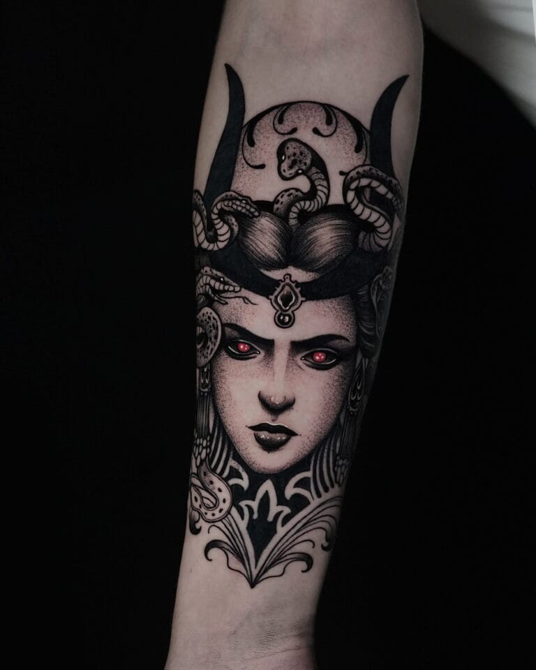 7sinstattoo.live Tatuaż o nazwie DSC06047 na przedramieniu, przedstawiający szczegółową Meduzę z utworzonymi zamiast włosów, misternym hełmem i świecącymi czerwonymi oczami na czarnym tle. Projekt wyróżnia się precyzyjną linią i cieniowaniem, tworząc mroczną, mityczną atmosferę. Najlepsze studio tatuażu Seven Sins Tattoo
