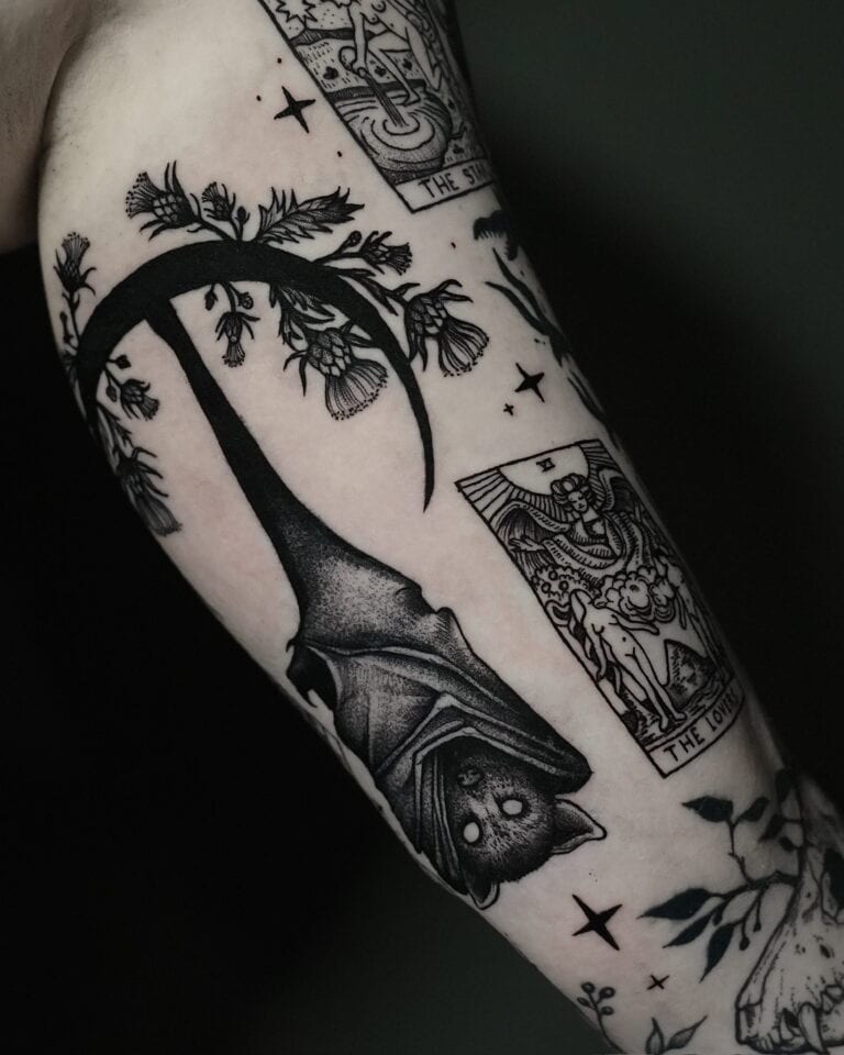 7sinstattoo.live Tatuaż na ramieniu wykonany w najlepszym studio tatuażu Poznań zawiera misterne wzory wykonane czarnym tuszem, w tym dużego nietoperza wiszącego do góry nogami, elementy kwiatowe i dwie karty tarota oznaczone jako „The Sun” i „The Lovers”. Obszar otaczający obejmuje liście i detale związane z naturą. To oszałamiające dzieło sztuki zostało uchwycone w produkcie DSC07762. Najlepsze studio tatuażu Seven Sins Tattoo
