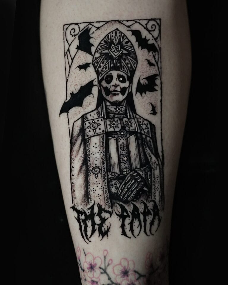 7sinstattoo.live Tatuaż na ramieniu osoby, uchwycony na zdjęciu DSC09857 ze studia tatuażu Poznań, przedstawia postać w wymyślnych szatach z nakryciem głowy, otoczoną nietoperzami. Wzór umieszczono w prostokątnej ramce. Pod postacią stylizowany tekst brzmi „The Toad”. Kwiaty wiśni zdobią dolną część ramienia. Najlepsze studio tatuażu Seven Sins Tattoo
