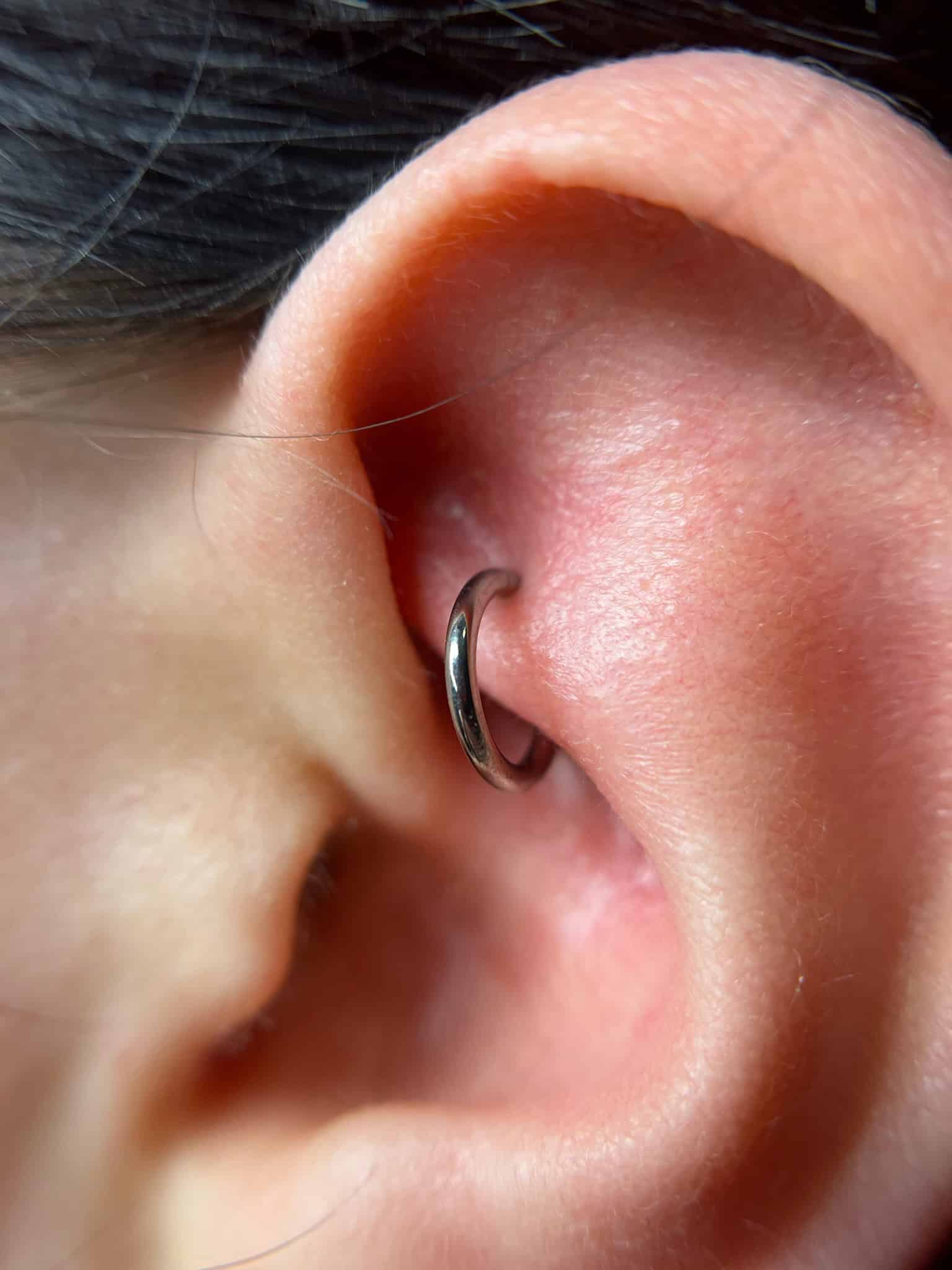 7sinstattoo.live Zbliżenie ucha osoby z małym, srebrnym kółkiem przebijającym tragus. Skóra wydaje się gładka, a kolczyk jest prosty i nieozdobiony — idealny pokaz minimalistycznej elegancji IMG_8950, często wykonywanej w najlepszym studio tatuażu Poznań. Najlepsze studio tatuażu Seven Sins Tattoo