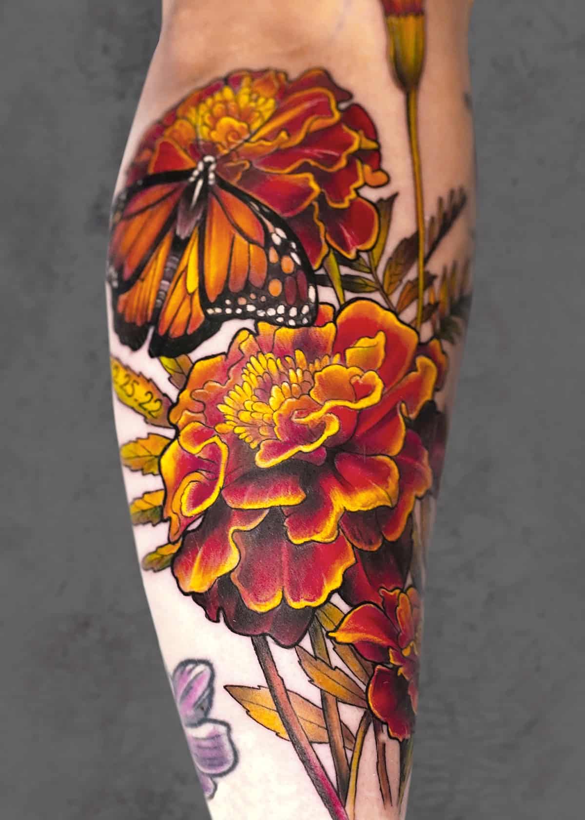 7sinstattoo.live Genialny tatuaż b2 na ramieniu osoby prezentuje żywe czerwone i żółte kwiaty z pieczołowicie wykonanymi płatkami, którym towarzyszy realistyczny pomarańczowy i czarny motyl monarcha siedzący na kwiatach. Ten skomplikowany wzór, mistrzowsko wykonany w tatuażu Poznań, wyróżnia się na jednolitym szarym tle. Najlepsze studio tatuażu Seven Sins Tattoo