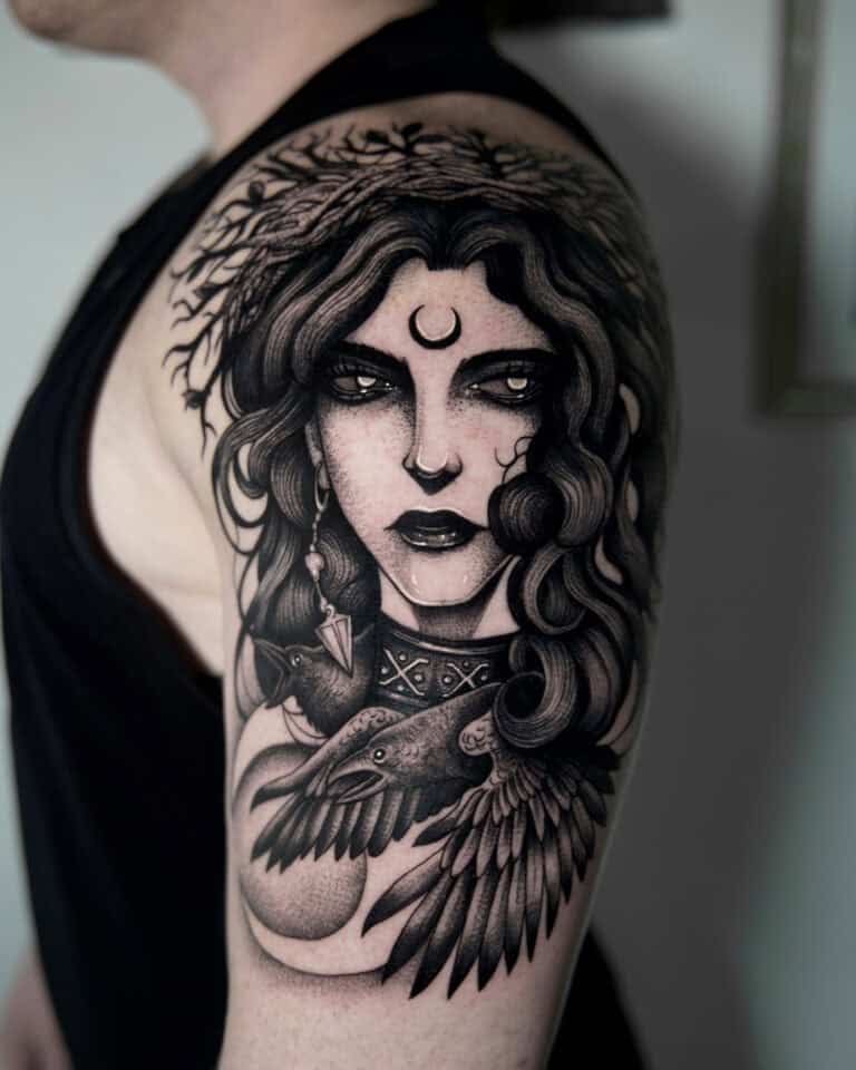 7sinstattoo.live Osoba ze szczegółowym czarno-szarym tatuażem na górnej części ramienia. Tatuaż „fggdh” Poznań przedstawia kobietę z długimi, falującymi włosami, półksiężycem na czole i dużym ptakiem, prawdopodobnie krukiem, na piersi — z misternym cieniowaniem i elementami wzornictwa. Najlepsze studio tatuażu Seven Sins Tattoo