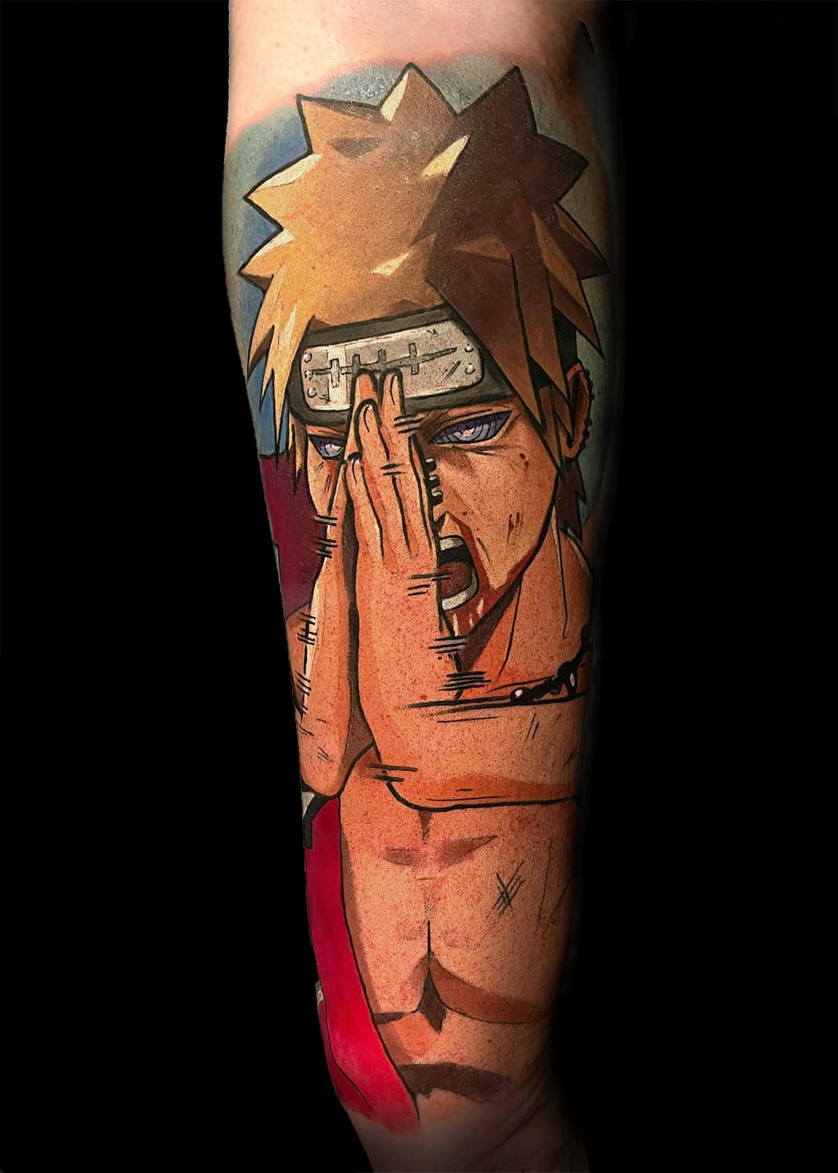 Tatuaż na przedramieniu przedstawia kolorowy obraz postaci z anime z kolczastymi blond włosami. Postać ma niebieskie oczy i nosi opaskę z metalową płytką. Postać pozuje z jedną ręką tworzącą znak dłoni przed twarzą, podczas gdy jej mięśnie klatki piersiowej i ramion są wyraźnie widoczne.