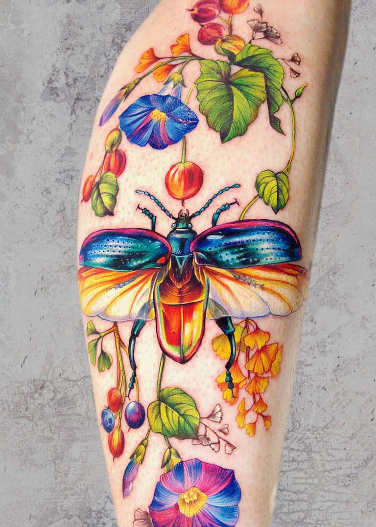 A Żywy tatuaż na przedramieniu, wykonany w Seven Sins Tattoo Poznań, przedstawia kolorowego chrząszcza z opalizującymi skrzydłami. Chrząszcz jest różnorodnymi jasnymi kwiatami i zielonymi składnikami, stanowiącymi żywy i szczegółowy wzór na jasnej rzeczywistości.