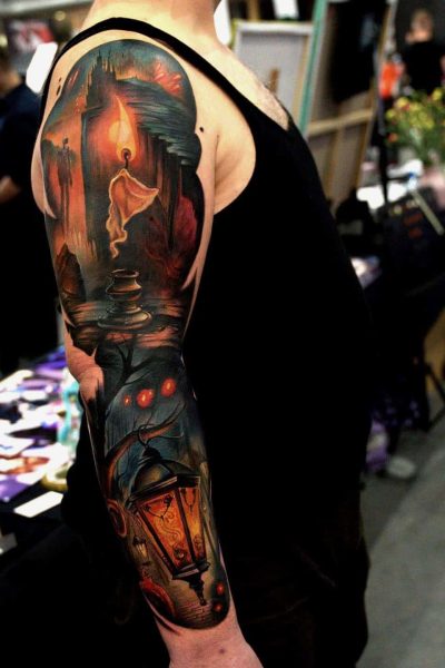 Mężczyzna ubrany w czarną koszulę bez rękawów przedstawia szczegółowy tatuaż na całym rękawie, wykonany przez zarządzane studio Seven Sins Tattoo w Poznaniu. Ten tatuaż przedstawia żywą, mistyczną scenę z lasem, jarzącą się latarnią, eteryczną strażą na ścieżce oraz mrocznymi, cieniastymi elementami.