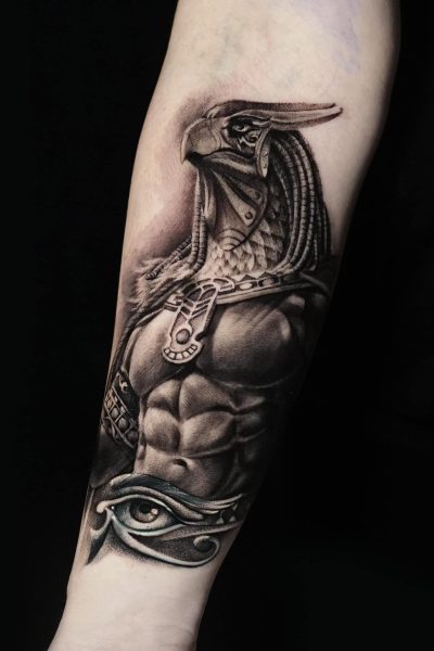 Wizualnie urzekający tatuaż z Seven Sins Tattoo w Poznaniu, przedstawiający muskularną humanoidalną postać z głową ptaka przypominającą starożytne egipskie bóstwo, zdobi przedramię. Szczegółowy element zawiera misterną zbroję i starożytne egipskie symbole, rozciągające się od połowy przedramienia do okolic łokcia, zidentyfikowane jako produkt 358142402_602998601950094_6270838721214934466_n. Ten mistrzowsko wykonany czarno-szary tatuaż to prawdziwe dzieło sztuki, które się wyróżnia.