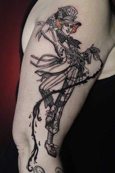 7sinstattoo.live Szczegółowy tatuaż na ramieniu przedstawia fantazyjną postać ubraną w strój vintage z cylindrem, muszką, kamizelką i spodniami w paski. Postać trzyma laskę i wydaje się być w trakcie tańca, otoczona misternymi elementami dekoracyjnymi, które wiją się wokół ramienia — prawdziwe arcydzieło ze studia tatuażu Poznań. Ta wyjątkowa grafika została uchwycona w produkcie DSC01336. Najlepsze studio tatuażu Seven Sins Tattoo