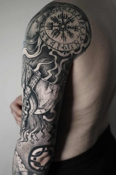7sinstattoo.live Górna część ramienia i bark osoby prezentujące misterny czarno-szary tatuaż ozdobiony symbolami nordyckimi, podkreślony Vegvisir (runiczny kompas) na ramieniu i różnymi innymi wzorami pokrywającymi całą długość ramienia. Ten element został wykonany w studio tatuażu Poznań, znanym jako najlepsze studio tatuażu Poznań. Proste, jasne tło dodaje idealnego kontrastu, aby podkreślić tę grafikę uchwyconą w DSC03395. Najlepsze studio tatuażu Seven Sins Tattoo