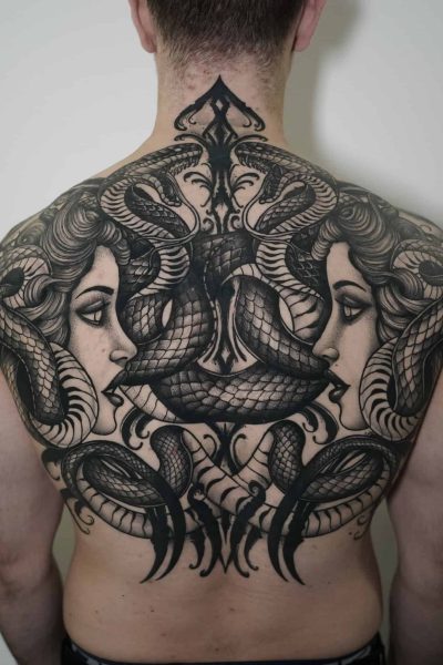 7sinstattoo.live Osoba z misternym, czarno-szarym tatuażem pokrywającym całe plecy, znana jako DSC03455, przedstawia dwie kobiety zwrócone ku sobie, otoczone splecionymi wężami, tworząc symetryczny i wyszukany wzór. To arcydzieło zostało wykonane przez artystę ze studia tatuażu Poznań. Najlepsze studio tatuażu Seven Sins Tattoo
