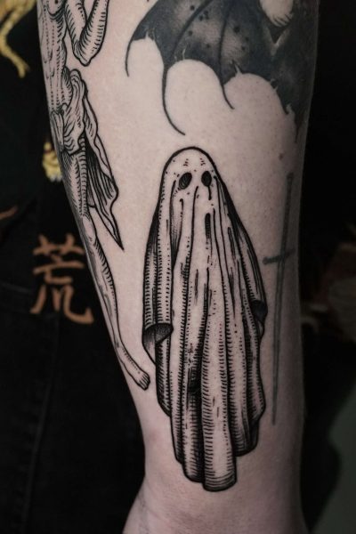 7sinstattoo.live Zbliżenie tatuażu z DSC04248, wykonanego w Najlepszym Studio Tatuażu Poznań, przedstawia czarno-białą, upiorną postać udrapowaną w zwiewnym prześcieradle z otworami na oczy. Wokół centralnego fragmentu znajdują się inne tatuaże o ciemnej tematyce, w tym szkieletowa postać i skrzydła nietoperza. Strój noszącego jest ozdobiony azjatyckimi wzorami postaci. Najlepsze studio tatuażu Seven Sins Tattoo