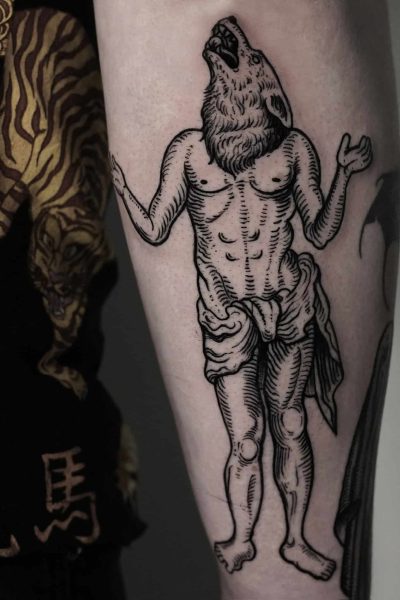 7sinstattoo.live Tatuaż uchwycony w DSC04263 na ramieniu przedstawia ludzkie ciało z głową wilka. Postać stoi z uniesionymi i lekko zgiętymi w łokciach ramionami. Wytatuowany w tatuaż Poznań, na ramieniu znajdują się również inne tatuaże, a osoba ma na sobie czarną koszulę ozdobioną żółto-białym wzorem.
 Najlepsze studio tatuażu Seven Sins Tattoo