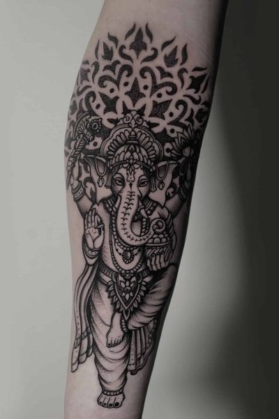 7sinstattoo.live Tatuaż na przedramieniu, przedstawiający czarno-szarą interpretację hinduskiego bóstwa z głową słonia, Ganeshy, prezentuje skomplikowany wzór o nazwie DSC04784. Został stworzony przez artystę z wiodącego studia tatuaży Poznań i zawiera ozdobne detale wokół bóstwa oraz elementy dekoracyjne nad głową Ganeshy. Najlepsze studio tatuażu Seven Sins Tattoo