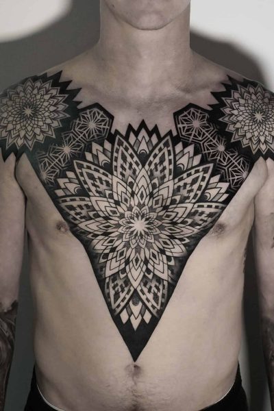 7sinstattoo.live Osoba z misternymi czarnymi geometrycznymi tatuażami pokrywającymi klatkę piersiową i ramiona, które zostały wykonane w najlepszym studio tatuażu w Poznaniu. Centralny wzór przedstawia duży, symetryczny wzór kwiatowy, podczas gdy mniejsze sąsiadujące wzory uzupełniają go na ramionach. Ta szczegółowa i symetryczna sztuka ciała została uchwycona w produkcie DSC04820. Najlepsze studio tatuażu Seven Sins Tattoo