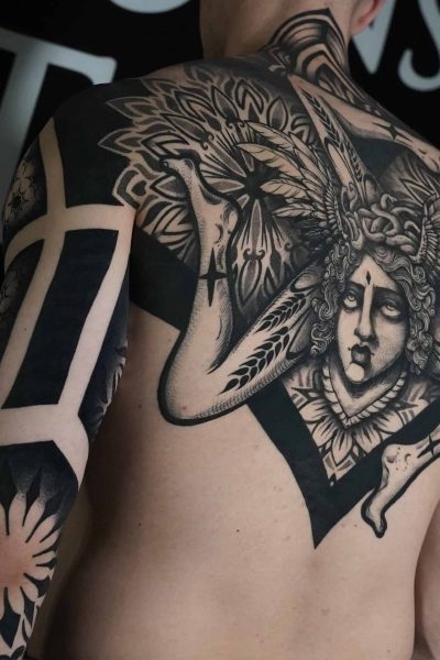 7sinstattoo.live Osoba z misternym tatuażem pokrywającym ramię i górną część pleców, wykonanym w studio tatuażu Poznań, prezentuje projekt DSC05919. Tatuaż przedstawia szczegółową twarz z misternym nakryciem głowy i ozdobnymi wzorami rozciągającymi się na ramieniu i ramieniu, obejmującymi śmiałe, geometryczne wzory i elementy kwiatowe. Najlepsze studio tatuażu Seven Sins Tattoo