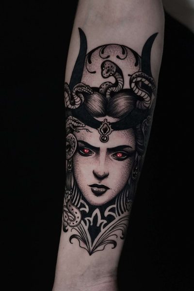 7sinstattoo.live Tatuaż o nazwie DSC06047 na przedramieniu, przedstawiający szczegółową Meduzę z utworzonymi zamiast włosów, misternym hełmem i świecącymi czerwonymi oczami na czarnym tle. Projekt wyróżnia się precyzyjną linią i cieniowaniem, tworząc mroczną, mityczną atmosferę. Najlepsze studio tatuażu Seven Sins Tattoo