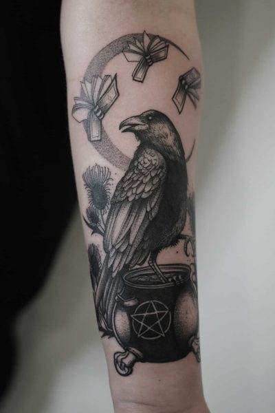 7sinstattoo.live Szczegółowy czarno-szary tatuaż (DSC08830ррр) na ramieniu przedstawia wronę siedzącą na kotle ozdobionym symbolem pentagramu. Nad wroną znajduje się zakrzywiony układ unoszących się książek, wszystko na tle roślin przypominających osty, które podkreślają mistyczny motyw. Ten misterny element został umiejętnie wykonany w Studio Tatuażu Poznań. Najlepsze studio tatuażu Seven Sins Tattoo