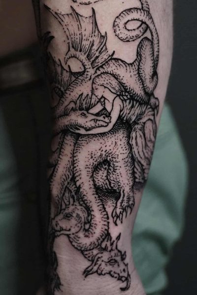 7sinstattoo.live Czarno-biały tatuaż oznaczony jako DSC09788 przedstawia dwa szczegółowe smoki splecione na przedramieniu człowieka. Smoki prezentują skomplikowane łuski i skrzydła, przy czym głowa jednego smoka jest skierowana do przodu, a drugiego do tyłu. Ten mistrzowsko wykonany element został stworzony w najlepsze studio tatuażu Poznań. Najlepsze studio tatuażu Seven Sins Tattoo