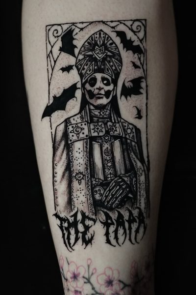 7sinstattoo.live Tatuaż na ramieniu osoby, uchwycony na zdjęciu DSC09857 ze studia tatuażu Poznań, przedstawia postać w wymyślnych szatach z nakryciem głowy, otoczoną nietoperzami. Wzór umieszczono w prostokątnej ramce. Pod postacią stylizowany tekst brzmi „The Toad”. Kwiaty wiśni zdobią dolną część ramienia. Najlepsze studio tatuażu Seven Sins Tattoo