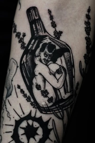 7sinstattoo.live W wyjątkowym pokazie artyzmu, DSC09899 przedstawia czarno-biały tatuaż na ramieniu, przedstawiający osobę zwiniętą w butelce, otoczoną elementami dekoracyjnymi, takimi jak kwiaty i abstrakcyjne kształty. Ten skomplikowany projekt podkreśla umiejętności tatuażysty Poznań w jednym z najlepszych studiów tatuażu Poznań. Najlepsze studio tatuażu Seven Sins Tattoo