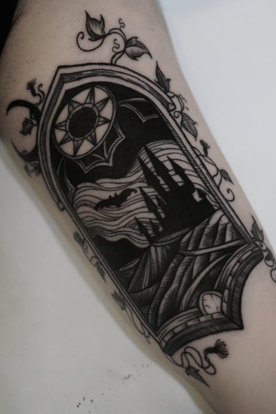 7sinstattoo.live Oszałamiający czarny tatuaż na skórze, oznaczony jako DSC09965, przedstawia gotyckie okno łukowe oplecione misternymi pnączami. W oknie ciemny zamek znajduje się na tle księżycowego nieba pełnego nietoperzy i chmur. Nad łukiem symbol słońca zapewnia uderzający kontrast z nocną sceną poniżej — prawdziwe arcydzieło tatuażysty Poznań w studio tatuażu Poznań. Najlepsze studio tatuażu Seven Sins Tattoo